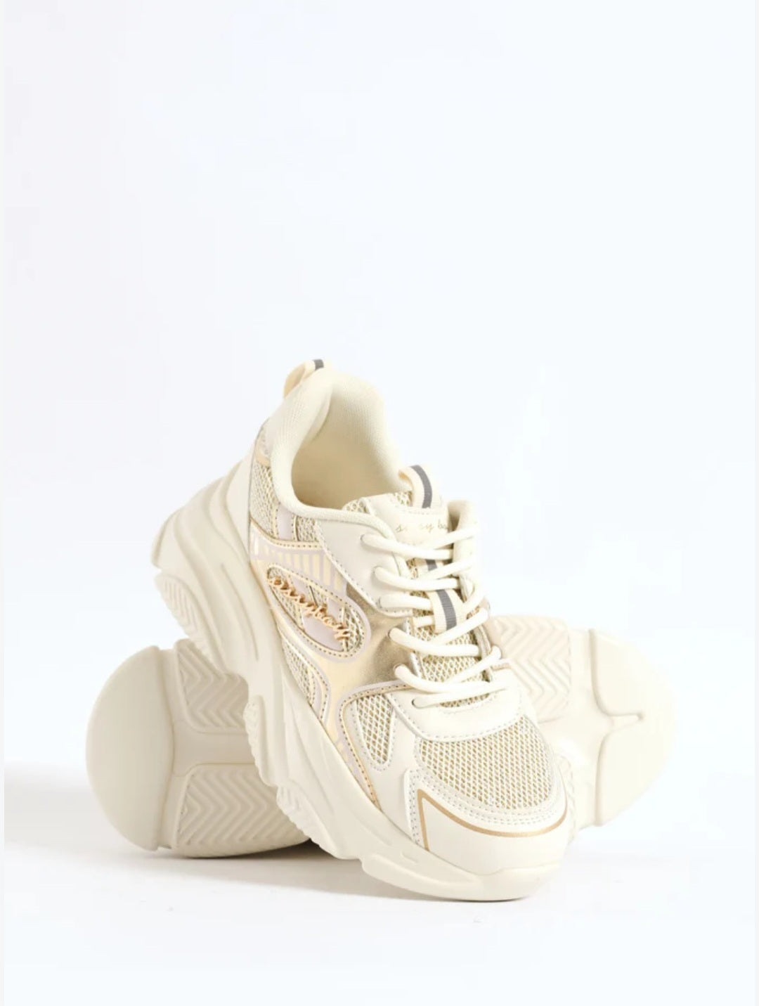A pair of chunky platform sneakers in a warm cream or off-white color, featuring mesh panels, thick sculpted soles, and lace-up fronts, set against a seamless white background.